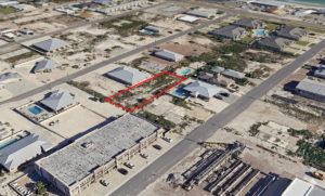 Aerial oblique view of a vacant lot outlined in red in a developed Florida Gulf Coast neighborhood, surrounded by residential homes and a commercial building, with paved streets visible on multiple sides.